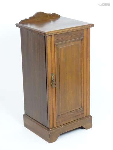 An early 20thC walnut bedside cabinet, with a shaped upstand and single fielded panelled door