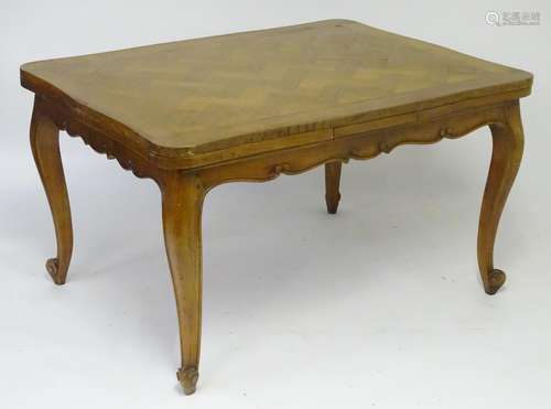 An early 20thC cherry wood dining table with a parquetry style top and draw leaves to each side,