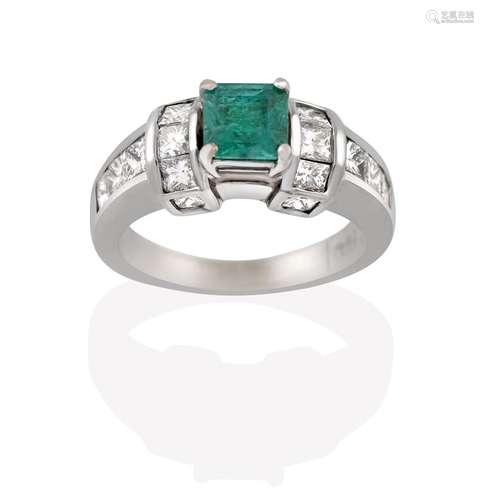 An Emerald and Diamond Ring, the emerald-cut emerald in a white four claw setting, flanked by a trio