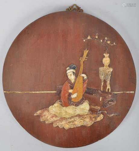 A Chinese wooden circular plaque inlaid with stone and marble with a figure playing a lute before a