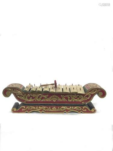 INDONESIA, painted wooden saron carved with rinceaux, bronze blades. Length: 94 cm. Width: 28 cm. Height: 26 cm. Wear and small accidents. A wooden and fabric mallet is attached. Height of the mallet : 16 cm.