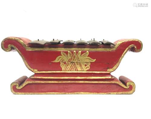 INDONESIA, wooden saron painted red and gold, flanked by two volutes decorated with scrolls and nets, the blades in metal. Length: 67 cm. Width: 27 cm. Height: 29 cm. Wear, accidents and oxidation. A wooden mallet is attached. Height of the mallet: 26 cm.