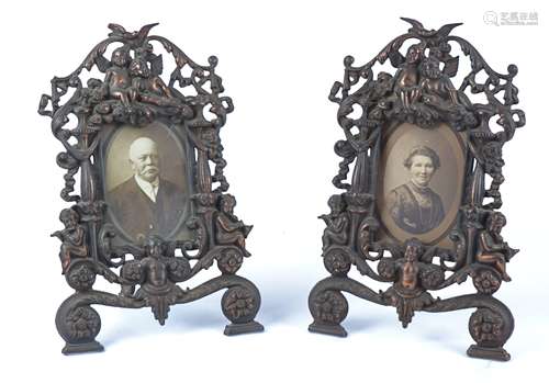 A pair of bronze effect mixed metal photograph frames with a surround of putti, 36cm x 23cm, one