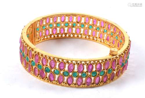 A decorative gilt bangle with semi precious red and green stones in the manner of rubies and