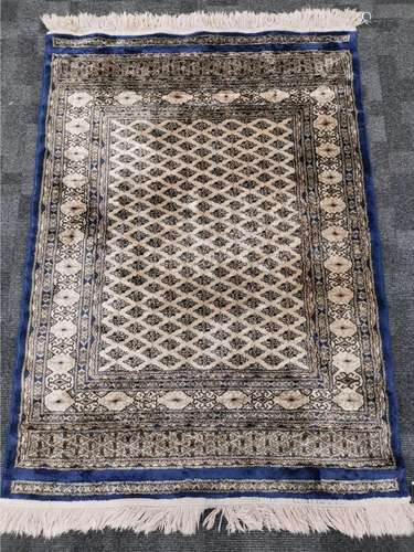 A Middle Eastern cream ground silk rug, with a blue border and repeating diamond pattern, tassels to