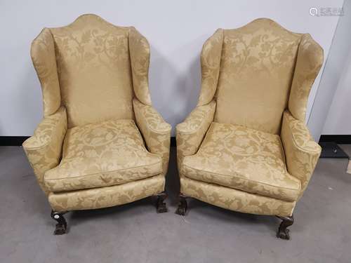 A pair of upholstered wing back arm chairs, set on claw and ball feet to the front. Floor to cushion