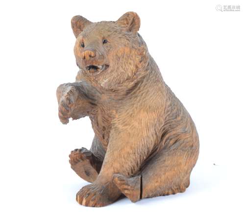 A Black Forest carved model of a seated bear, with one paw raised and black glass eyes, height