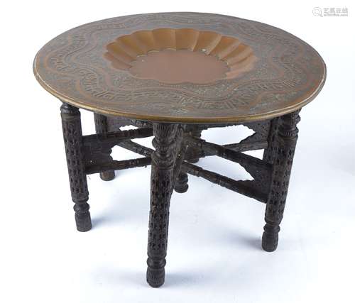 An Eastern embossed copper circular tray top table, raised on a six carved wooden legs, diameter