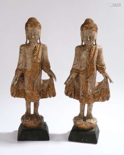Pair of carved wooden standing buddha figures, with gilt decoration, raised on tapering black bases,