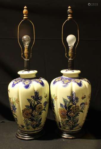 A pair of large lobed ovoid Delft style lamp bases, painted with leafy foliage, ebonised circular