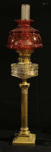 An early 20th century oil lamp, brass Corinthian column, clear glass reservoir, cranberry glass