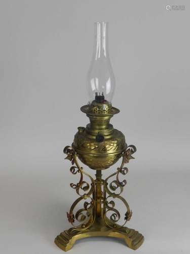 An Edwardian brass oil lamp, with embossed reservoir raised on scroll supports and a trefoil base,