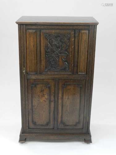 An Edwardian oak collector's or music cabinet, the single carved panelled door opening to an