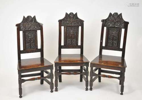 A set of three 17th century oak chairs, each with a foliate carved cresting rail, above a panelled