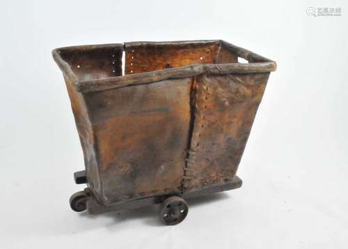 An unusual rustic sewn hide laundry cart, on a wooden frame and iron wheels, 84cm high, 96 x 56cm.