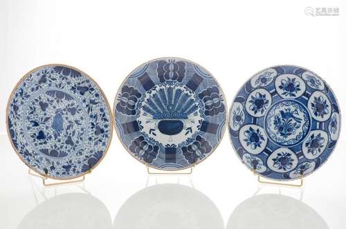 DELFT. Lot de trois assiettes en faïence émaillée bleu blanc, l'une à décor d'un vase fleuri à la queue de paon, l'un à décor de fleurs et d'un oiseau dans des cartouches, l'une à décor d'un semis de fleurs et rinceaux. Marques au revers. XVIIIème siècle, diverses manufacrures dont la Griffe de Porcelaine (Diam : 23,5 cm) (petites égrenures)