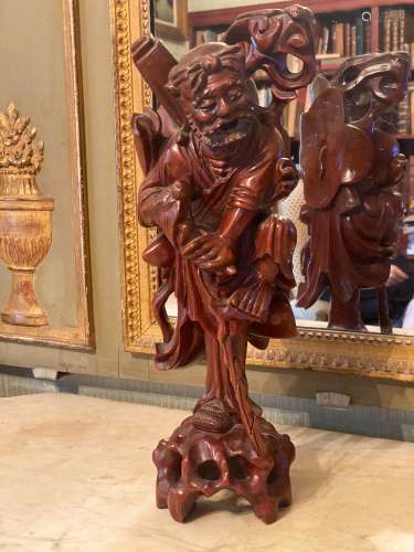 中国，19世纪末。老石雕像脚踏如意杖，站立在如意杖上。他拿着一根球棒。 在他的背上，我们注意到一个卷轴，一个花瓶，一个蝙蝠，在背上的下部是一朵莲花。木头。高度：39厘米。裂缝和破胶。