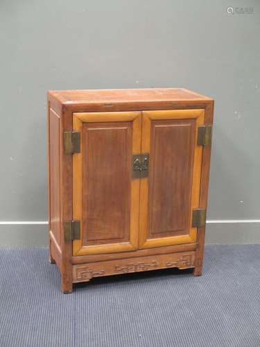 A Chinese two-coloured wood cupboard, early 20th century, of two cupboard doors over a carved apron,