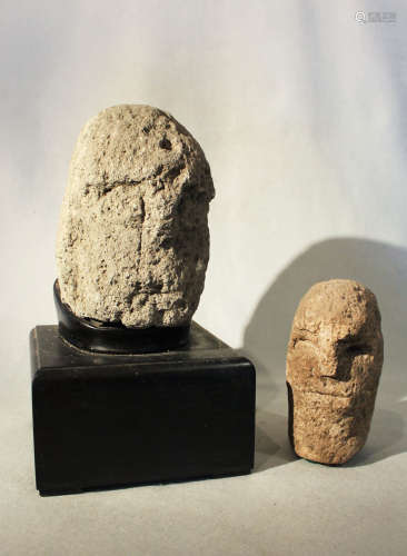 A carved tufa primitive head, perhaps early Chinese, and another smaller example, 21cm and 17cm (2)
