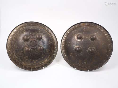 Two Indian dhals of convex form with four central bosses and reinforced brim, the ground decorated