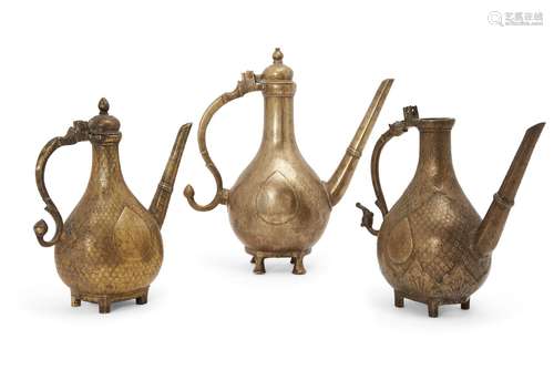 Three Mughal engraved brass ewers, 18th century India, each of pear shape on four feet, with