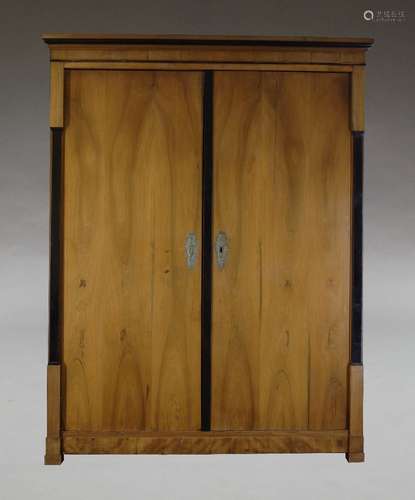 A Biedermeier cherry wood and ebonised wardrobe, early 19th Century, the moulded cornice above two