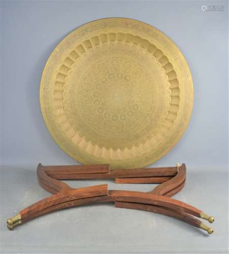 A Middle Eastern brass table top, on a wooden folding base, 71cm diameter.