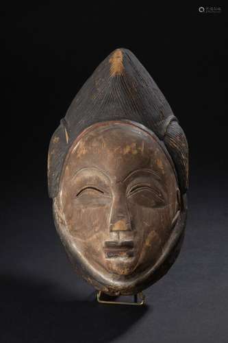 Masque Punu, Gabon H. 31 cm Finesse des traits et sérénité accentués par les fines incisions du regard en croissant de lune inversé créant une force d'intériorité. Les arcades sourcilières délicatement tracées. Le pourtour du front légèrement bombé est délimité par une Subtile  démarcation rouge partant des tempes annonçant une Jolie coiffe sommitale peignée.