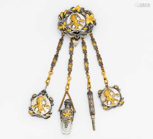 CHATELAINE. Germany. 1900s. Silver, gildet, glass, total weight: ca. 105,5 g. 23,2 x 6,5 cm. Chatelaine with 4 strands. 1. blackboard, 2. pen, 3. bottle, 4. mirror. Motif with woman's head and floral patterns. hallmark H.+G.GESCH. Chatlaine in good condition. Silver tarnishing in a few places. Slightly scratched in a few places. Mirror blind.