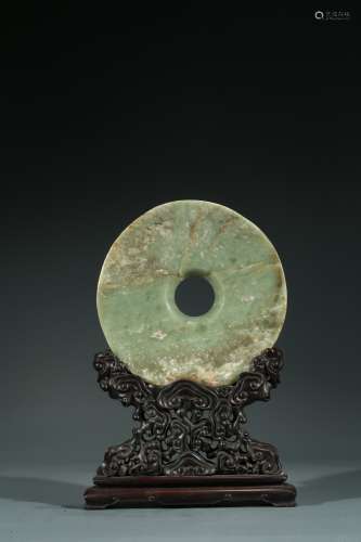 A CHINESE CELADON JADE DISC WITH HARDWOOD STAND