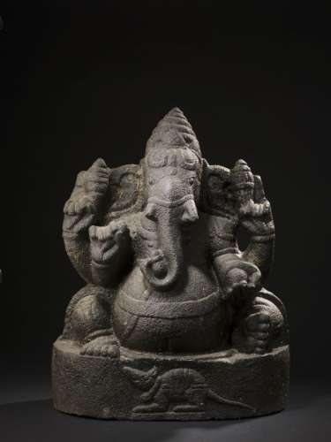 印度，十六至十八世纪黑色火山石的格涅沙雕像。H.52.5厘米后部这尊雕像代表着象头神Ganesh，是最受欢迎的印度教神灵之一。在他的脚下，可以看到作为他的交通工具（或瓦哈纳）的Mushika老鼠。他是消除障碍、赐予成功的神。他也是'起点'的主宰。在任何旅程或项目开始时，都会求助于他的帮助。因为他的动物头颅，Ganesh可能是一个万物有灵论的神，后来被吸收到印度万神殿中。关于他的出身，有很多故事。他被认为是湿婆和帕瓦蒂的两个儿子之一。与他的起源有关的故事说，他是由他的母亲或父亲单独创造的。关于他的象头是如何得到的，也有很多解释。他的名字的意思是主神或Ganas，圆形的矮人是湿婆的仆人。几乎所有的寺庙都有格涅沙的图像，通常放置在十字路口或上面的大门或访问，特别是在寺庙里献给他的父亲，湿婆。神的形象也出现在国内许多祭坛的显著位置。