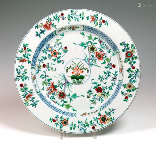 青花系瓷器中的圆盘。中国，18世纪。中间装饰着各种红色的花朵和绿色植物的奖章，周围是交错的花朵图案。  边缘由蓝色几何图案的对称花牌组成。翅膀上装饰着花和叶子。直径：38.9厘米 纹理，背面有裂纹。