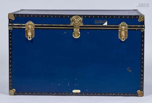 A BRASS BOUND BLUE REXINE COVERED PLY TRUNK WITH BLACK PLASTIC STUDDED BORDERS, LACQUERED GILT WHITE