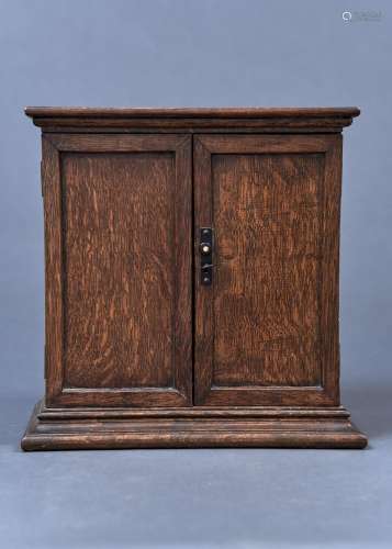 AN OAK SMOKER'S CABINET, C1920, ENCLOSED BY A PAIR OF PANELLED DOORS, THE INTERIOR WITH OPEN
