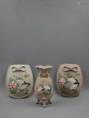 中国，1970年代。牡丹中的仙鹤装饰的一对烛台花瓶。彩绘灰陶装饰，珐琅部位浮雕彩绘。背面盖章。高度：12厘米。附上的是一个小荷包形的花瓶，搁在儿童形成的三只脚上。腹部以浅浮雕的方式装饰着花草和仙鹤。部分上釉的灰色赤土。高度11.5厘米。印章