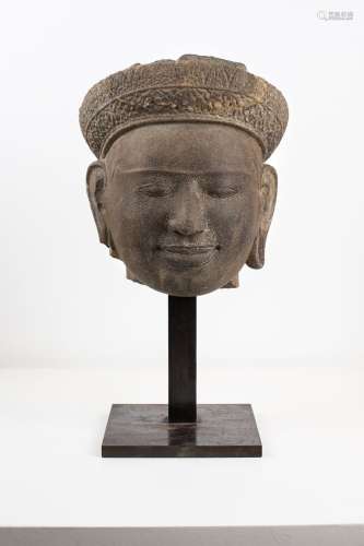 柬埔寨，12世纪的高棉艺术。高棉艺术中典型的笑容甜美的男神头像，背后系着银色头饰。鬓角之上，可见刻画精致的发绺。耳朵的亭子被雕刻成花瓣的形状。头顶原本是一个高高的竖髻。灰色砂岩。高度：21厘米。恢复了头饰的中央部分。