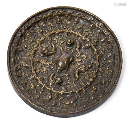 A Chinese bronze 'lion and grape' mirror, Tang dynasty, cast with a central lion-shaped loop