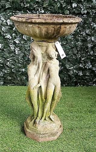 A reconstituted stone bird bath, the fluted reservoir on a pedestal relief cast as the three Graces,