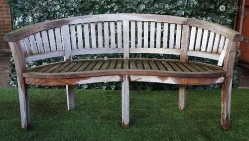 A teak framed semi-elliptic garden bench with slatted back and seat, on block supports,