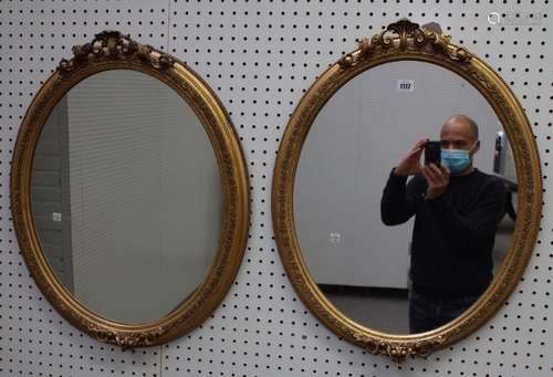 A pair of gilt framed oval wall mirrors with floral chased frames, 55cm wide x 61cm high, (2).