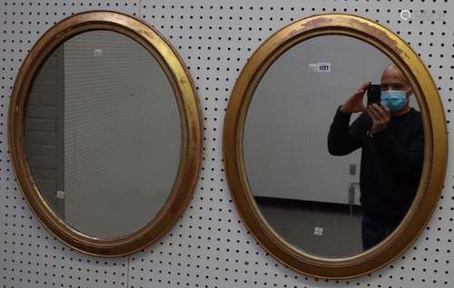 A pair of early 20th century gilt framed oval wall mirrors, with bead mounted frames,