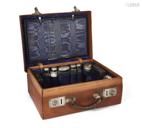 A leather travelling vanity case, fitted with hammered white metal mounted glass vanity jars (