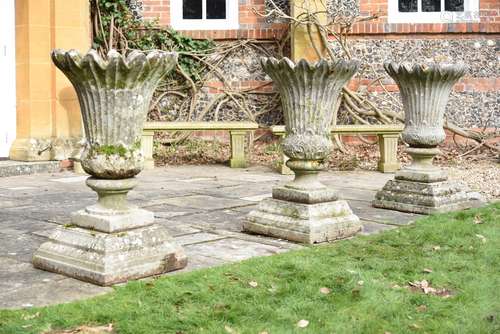 A set of three stone composition garden urns on plinths