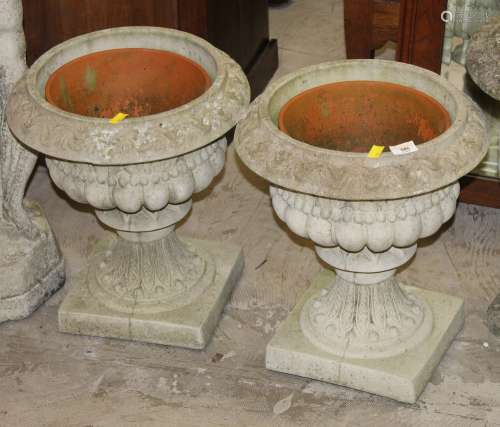 A pair of cast composite stone garden urns with stylized mou...
