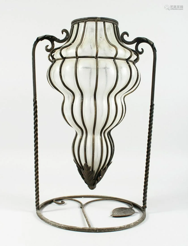 A FOUR TIER TINTED SHAPED GLASS VASE on a wrought iron