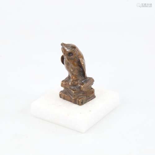 A miniature patinated bronze owl seated on books, on white m...