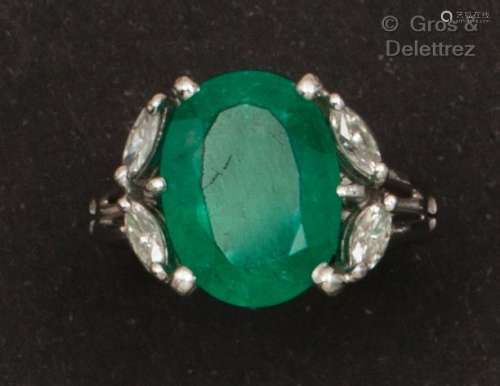 一枚白金戒指，镶嵌着一颗椭圆形祖母绿和四颗脐带式切割钻石。手指...