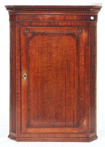 A George III oak hanging corner cupboard, the flared dentil ...