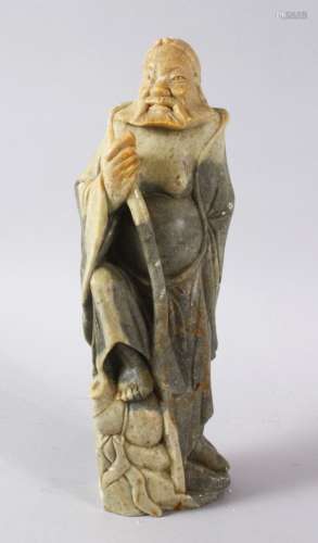 A LARGE CHINESE SOAPSTONE CARVING OF AN IMMORTAL, stood upon...