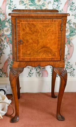 A FIGURED WALNUT BEDSIDE CUPBOARD with panel doors, on cabri...